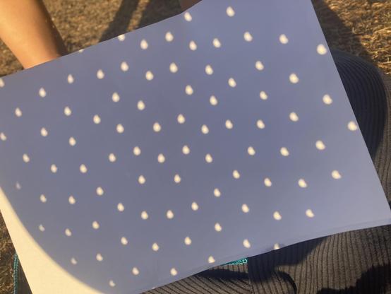 Dozens of small dots projected onto a sheet of paper. The dots are slightly deformed because the moon has eaten into the sun disc at that point.
